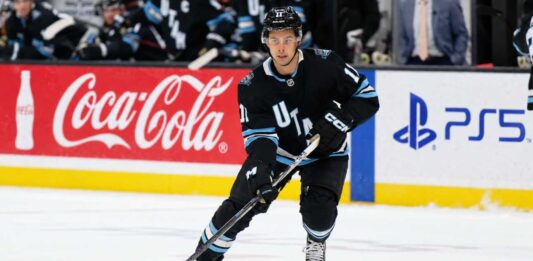 Dylan Guenther Point Projections 2026-27: Utah Mammoth Fantasy Outlook Dylan Guenther skating for the Utah Mammoth beside Coca-Cola and PS5 board ads in a 2026-27 fantasy hockey point projection.