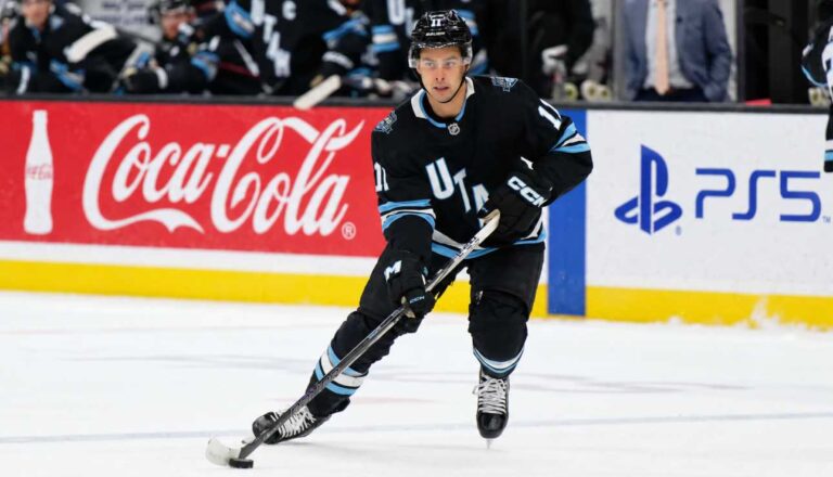 Dylan Guenther skating for the Utah Mammoth beside Coca-Cola and PS5 board ads in a 2026-27 fantasy hockey point projection.
