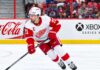 Dylan Larkin Trade Rumors: Did His Expanded Trade List Just Change Everything? Dylan Larkin skating for the Detroit Red Wings amid NHL trade rumors, with Colorado Avalanche fans in the stands and Coca-Cola and Xbox Series X ads on the boards.