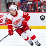 Dylan Larkin Trade Rumors: Did His Expanded Trade List Just Change Everything? Dylan Larkin skating for the Detroit Red Wings amid NHL trade rumors, with Colorado Avalanche fans in the stands and Coca-Cola and Xbox Series X ads on the boards.