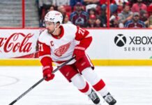 Dylan Larkin Trade Rumors: Did His Expanded Trade List Just Change Everything? Dylan Larkin skating for the Detroit Red Wings amid NHL trade rumors, with Colorado Avalanche fans in the stands and Coca-Cola and Xbox Series X ads on the boards.