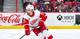 Dylan Larkin Trade Rumors: Did His Expanded Trade List Just Change Everything? Dylan Larkin skating for the Detroit Red Wings amid NHL trade rumors, with Colorado Avalanche fans in the stands and Coca-Cola and Xbox Series X ads on the boards.