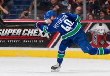 Elias Pettersson of the Vancouver Canucks takes a powerful shot in action as a Super Chexx bubble hockey board ad appears behind him amid Los Angeles Kings trade rumors.