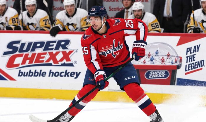 jordan-kyrou-washington-capitals-fantasy-hockey-2026-27 Jordan Kyrou in a Washington Capitals home jersey skates with the puck in front of a stylish Super Chexx bubble hockey boards ad and Pittsburgh Penguins bench