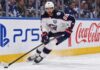 Montreal Canadiens Trade Rumors: Could Kirill Marchenko Be Traded Before Opening Night? Kirill Marchenko skating for the Columbus Blue Jackets beside PS5 and Coca-Cola board ads amid Montreal Canadiens trade rumors.