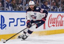 Montreal Canadiens Trade Rumors: Could Kirill Marchenko Be Traded Before Opening Night? Kirill Marchenko skating for the Columbus Blue Jackets beside PS5 and Coca-Cola board ads amid Montreal Canadiens trade rumors.
