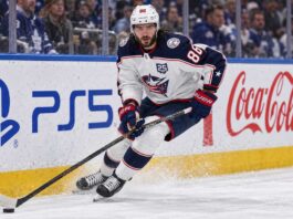 Kirill Marchenko skating for the Columbus Blue Jackets beside PS5 and Coca-Cola board ads amid Montreal Canadiens trade rumors.