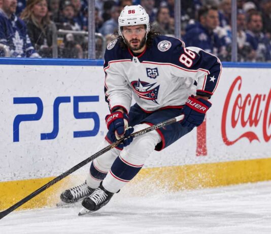 Kirill Marchenko skating for the Columbus Blue Jackets beside PS5 and Coca-Cola board ads amid Montreal Canadiens trade rumors.