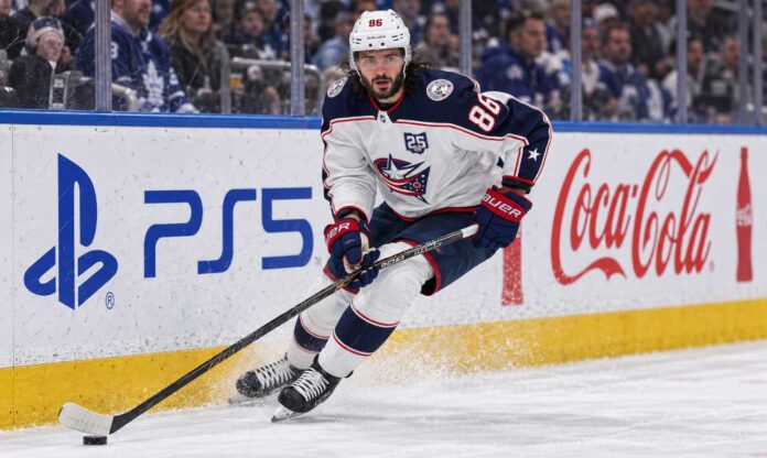 kirill-marchenko-montreal-canadiens-trade-rumors-blue-jackets Kirill Marchenko skating for the Columbus Blue Jackets beside PS5 and Coca-Cola board ads amid Montreal Canadiens trade rumors.