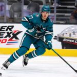 Michael Misa Point Projections 2026-27: San Jose Sharks Fantasy Outlook Michael Misa skating for the San Jose Sharks beside a Super Chexx Pro bubble hockey board ad in a 2026-27 fantasy hockey point projection.
