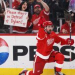 NHL News and NHL Rumors Today: Trade Buzz, Injuries and NHL Scores – September 26, 2026 Detroit Red Wings captain Dylan Larkin celebrates on one knee in front of cheering fans, including a female fan holding a “Please stay in Detroit Dylan!” sign, with a Pepsi board ad in the background.