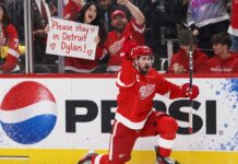 NHL News and NHL Rumors Today: Trade Buzz, Injuries and NHL Scores – September 26, 2026 Detroit Red Wings captain Dylan Larkin celebrates on one knee in front of cheering fans, including a female fan holding a “Please stay in Detroit Dylan!” sign, with a Pepsi board ad in the background.