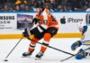 Quinn Hughes Trade Rumors: Could the Philadelphia Flyers Beat the Devils to the Wild Superstar? Quinn Hughes in a Philadelphia Flyers home uniform during NHL trade rumor speculation, with Samsung TV and Apple iPhone rink board ads in the background