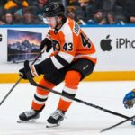 Quinn Hughes Trade Rumors: Could the Philadelphia Flyers Beat the Devils to the Wild Superstar? Quinn Hughes in a Philadelphia Flyers home uniform during NHL trade rumor speculation, with Samsung TV and Apple iPhone rink board ads in the background