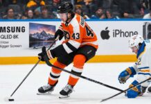 Quinn Hughes Trade Rumors: Could the Philadelphia Flyers Beat the Devils to the Wild Superstar? Quinn Hughes in a Philadelphia Flyers home uniform during NHL trade rumor speculation, with Samsung TV and Apple iPhone rink board ads in the background