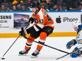 Quinn Hughes Trade Rumors: Could the Philadelphia Flyers Beat the Devils to the Wild Superstar? Quinn Hughes in a Philadelphia Flyers home uniform during NHL trade rumor speculation, with Samsung TV and Apple iPhone rink board ads in the background