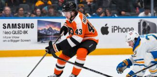 Quinn Hughes Trade Rumors: Could the Philadelphia Flyers Beat the Devils to the Wild Superstar? Quinn Hughes in a Philadelphia Flyers home uniform during NHL trade rumor speculation, with Samsung TV and Apple iPhone rink board ads in the background