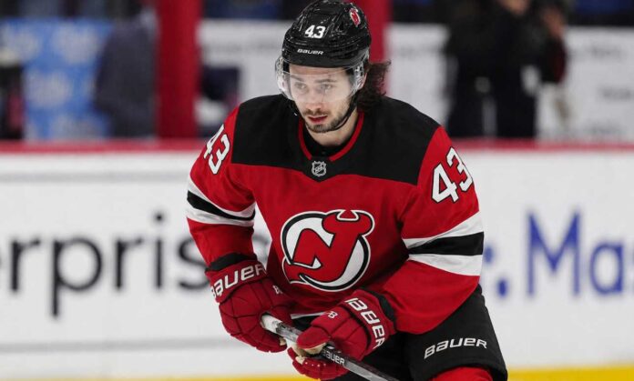 quinn-hughes-wild-devils-trade-rumors-2026 Quinn Hughes wearing a New Jersey Devils home jersey amid NHL trade rumors involving the Minnesota Wild and New Jersey Devils.