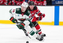 Quinn Hughes of the Minnesota Wild skates with the puck as a New Jersey Devils player pressures him during NHL action amid Quinn Hughes trade rumors