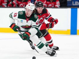 Quinn Hughes of the Minnesota Wild skates with the puck as a New Jersey Devils player pressures him during NHL action amid Quinn Hughes trade rumors