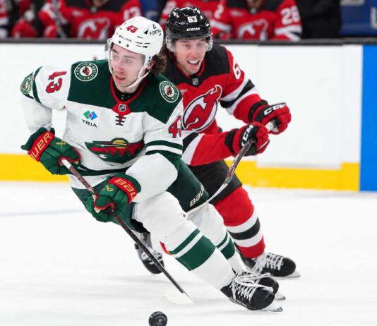 Quinn Hughes of the Minnesota Wild skates with the puck as a New Jersey Devils player pressures him during NHL action amid Quinn Hughes trade rumors