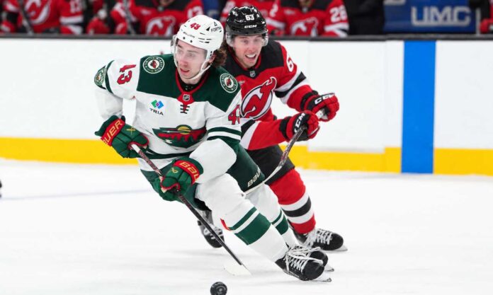 Quinn Hughes of the Minnesota Wild skates with the puck as a New Jersey Devils player pressures him during NHL action amid Quinn Hughes trade rumors