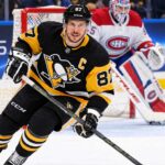 Sidney Crosby Trade Rumors: Did He Just Close the Door on a Canadiens or Avalanche Blockbuster? Sidney Crosby skating in a Pittsburgh Penguins home jersey with a Montreal Canadiens goalie in the background and a PS5 rink-board advertisement.