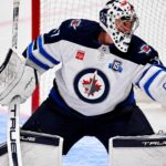 Connor Hellebuyck Trade Rumors: Is Utah About to Beat Buffalo to Winnipeg’s Star Goalie? Connor Hellebuyck of the Winnipeg Jets in his white away jersey making a save as NHL trade rumors link the star goaltender to the Buffalo Sabres and Utah Mammoth ahead of the October 23 decision.