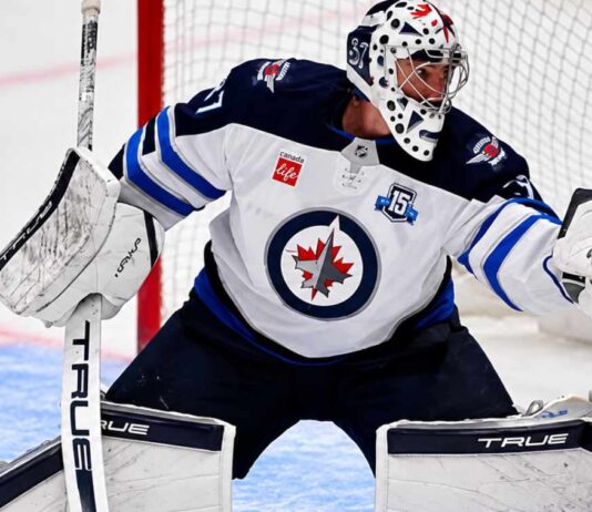 Connor Hellebuyck of the Winnipeg Jets in his white away jersey making a save as NHL trade rumors link the star goaltender to the Buffalo Sabres and Utah Mammoth ahead of the October 23 decision.
