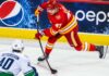 Calgary Flames forward Connor Zary (#47) skating with the puck against Vancouver Canucks Elias Pettersson in an away jersey, with a Pepsi advertisement on the boards, amid NHL trade rumors linking Zary to Vancouver.