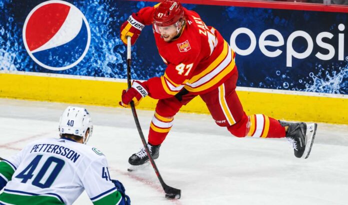 connor-zary-vancouver-canucks-calgary-flames-trade-rumors-2026 Calgary Flames forward Connor Zary (#47) skating with the puck against Vancouver Canucks Elias Pettersson in an away jersey, with a Pepsi advertisement on the boards, amid NHL trade rumors linking Zary to Vancouver.