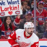 Dylan Larkin Trade Rumors: Did Montreal Just Give Him a Reason to Reconsider? Detroit Red Wings captain Dylan Larkin skates in his white away jersey as Montreal Canadiens fans cheer behind him, including a fan holding a "We Want Larkin!" sign amid NHL trade rumors.