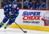 Elias Pettersson Trade Rumors: Did His Hot Start Just Change Vancouver’s Plans? Elias Pettersson skating along the boards in a Vancouver Canucks jersey beside a Super Chexx Bubble Hockey advertisement amid NHL trade rumors following his hot start to the 2026-27 season.