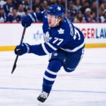 Maple Leafs Explored Simon Edvinsson Trade: Did Detroit Just Shut the Door? Simon Edvinsson wearing a Toronto Maple Leafs home jersey in a concept image, skating in front of Leafs fans amid NHL trade rumors involving the Detroit Red Wings.