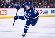 Maple Leafs Explored Simon Edvinsson Trade: Did Detroit Just Shut the Door? Simon Edvinsson wearing a Toronto Maple Leafs home jersey in a concept image, skating in front of Leafs fans amid NHL trade rumors involving the Detroit Red Wings.