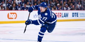 Simon Edvinsson wearing a Toronto Maple Leafs home jersey in a concept image, skating in front of Leafs fans amid NHL trade rumors involving the Detroit Red Wings.