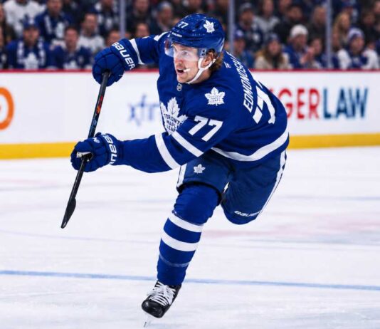 Simon Edvinsson wearing a Toronto Maple Leafs home jersey in a concept image, skating in front of Leafs fans amid NHL trade rumors involving the Detroit Red Wings.