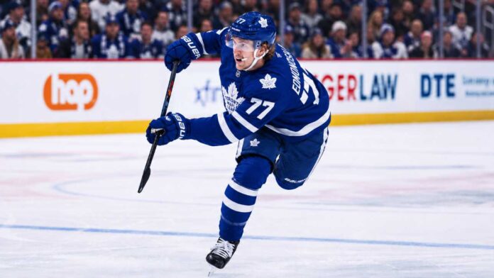 maple-leafs-simon-edvinsson-detroit-red-wings-trade-rumors-2026 Simon Edvinsson wearing a Toronto Maple Leafs home jersey in a concept image, skating in front of Leafs fans amid NHL trade rumors involving the Detroit Red Wings.