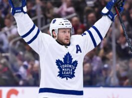 Morgan Rielly wearing a white Toronto Maple Leafs away jersey and helmet as NHL trade rumors intensify following reports that the Leafs struggled to find a trade partner for the veteran defenseman.