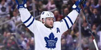 Maple Leafs Tried to Trade Morgan Rielly: Insider Reveals Why Nobody Bit Morgan Rielly wearing a white Toronto Maple Leafs away jersey and helmet as NHL trade rumors intensify following reports that the Leafs struggled to find a trade partner for the veteran defenseman.