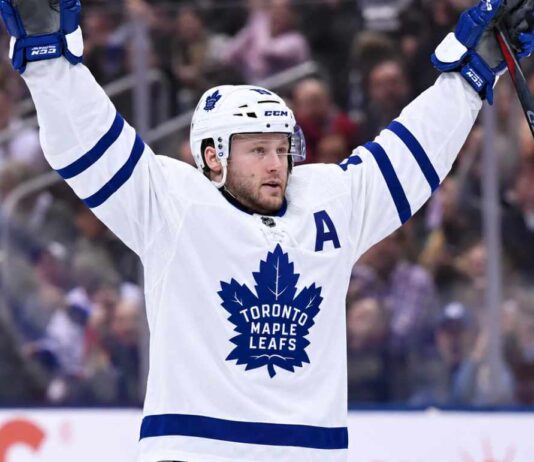 Morgan Rielly wearing a white Toronto Maple Leafs away jersey and helmet as NHL trade rumors intensify following reports that the Leafs struggled to find a trade partner for the veteran defenseman.