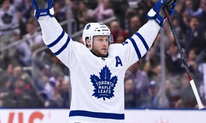 morgan-rielly-toronto-maple-leafs-trade-rumors-2026 Morgan Rielly wearing a white Toronto Maple Leafs away jersey and helmet as NHL trade rumors intensify following reports that the Leafs struggled to find a trade partner for the veteran defenseman.