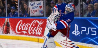 New York Rangers goalie Igor Shesterkin in action as a female Rangers fan holds a "Get well soon Igor!" sign behind the glass, following his season-ending injury. Coca-Cola and PS5 advertisements line the boards.