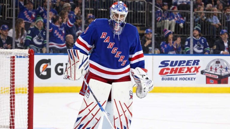 New York Rangers goalie Igor Shesterkin in front of his net with Gatorade and Super Chexx Bubble Hockey board ads and Canucks and Rangers fans in the stands.