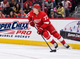 Simon Edvinsson skates for the Detroit Red Wings beside a Super Chexx Pro Bubble Hockey ad amid NHL trade rumors.