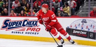 Simon Edvinsson skates for the Detroit Red Wings beside a Super Chexx Pro Bubble Hockey ad amid NHL trade rumors.