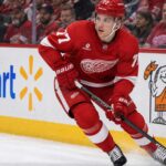 Simon Edvinsson Trade Rumors: Did the Flyers’ Nightmare Start Just Accelerate a Blockbuster? Simon Edvinsson skating for the Detroit Red Wings amid Philadelphia Flyers trade rumors, with Walmart and Little Caesars ads on the boards.