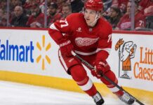 Simon Edvinsson Trade Rumors: Did the Flyers’ Nightmare Start Just Accelerate a Blockbuster? Simon Edvinsson skating for the Detroit Red Wings amid Philadelphia Flyers trade rumors, with Walmart and Little Caesars ads on the boards.