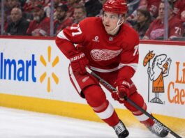 Simon Edvinsson skating for the Detroit Red Wings amid Philadelphia Flyers trade rumors, with Walmart and Little Caesars ads on the boards.