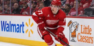 Simon Edvinsson Trade Rumors: Did the Flyers’ Nightmare Start Just Accelerate a Blockbuster? Simon Edvinsson skating for the Detroit Red Wings amid Philadelphia Flyers trade rumors, with Walmart and Little Caesars ads on the boards.